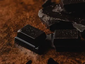 Dunkle Schokolade liegt zerbrochen auf einer Holzunterlage.