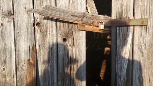 Kaputte Holztür mit Vorhängeschloss, Schatten sichtbar.