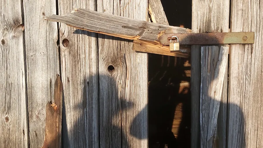 Kaputte Holztür mit Vorhängeschloss, Schatten sichtbar.