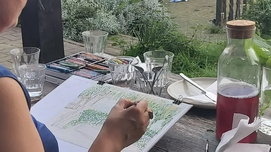 Person zeichnet draußen auf Holztisch.