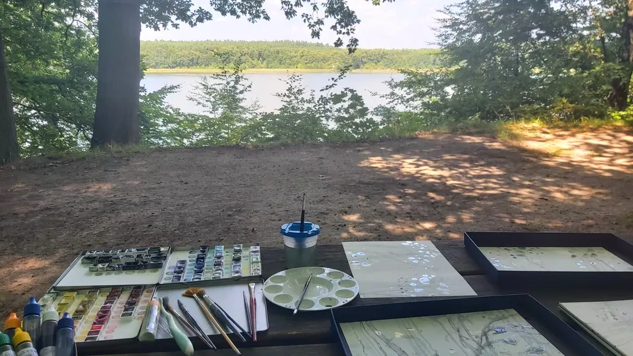 Painting supplies on table overlooking forest lake.