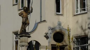 Statue einer historischen Figur vor Gebäudefassade.