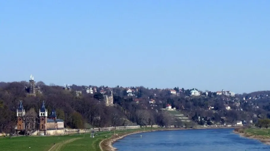 River flows beside hillside with buildings.