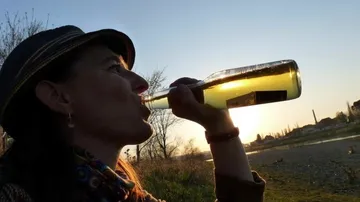Person drinking beer outdoors at sunset.