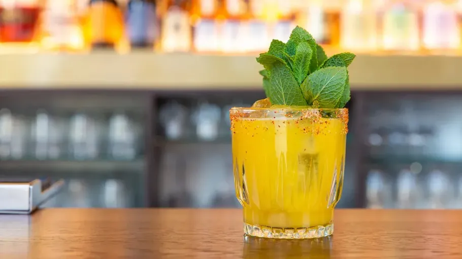 Yellow cocktail with mint on bar counter.