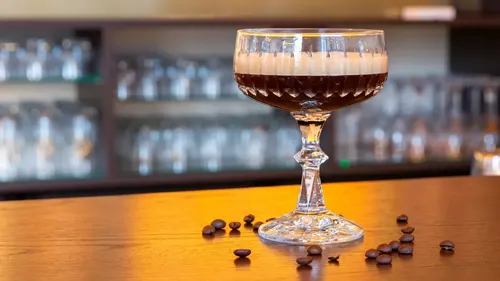 Cocktail glass with layers on bar counter.