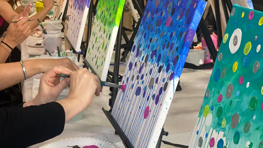 People painting colorful dot scenes on canvases.