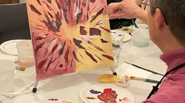 Person malt abstrakte Kunst auf Staffelei drinnen.