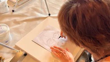 Person zeichnet auf Papier an einem Tisch.