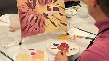 Person malt abstrakte Kunst am Tisch.