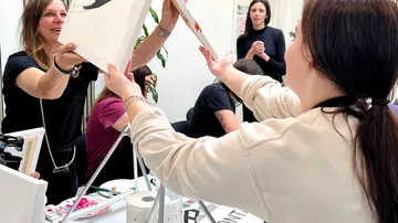 Zwei Frauen tauschen Gemälde bei Workshop aus.