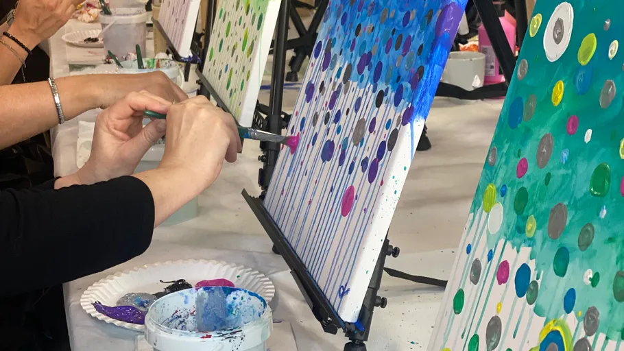 Hands painting colorful dotted canvases indoors.