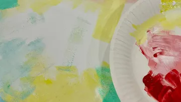 Paint-streaked paper plate on colorful canvas.