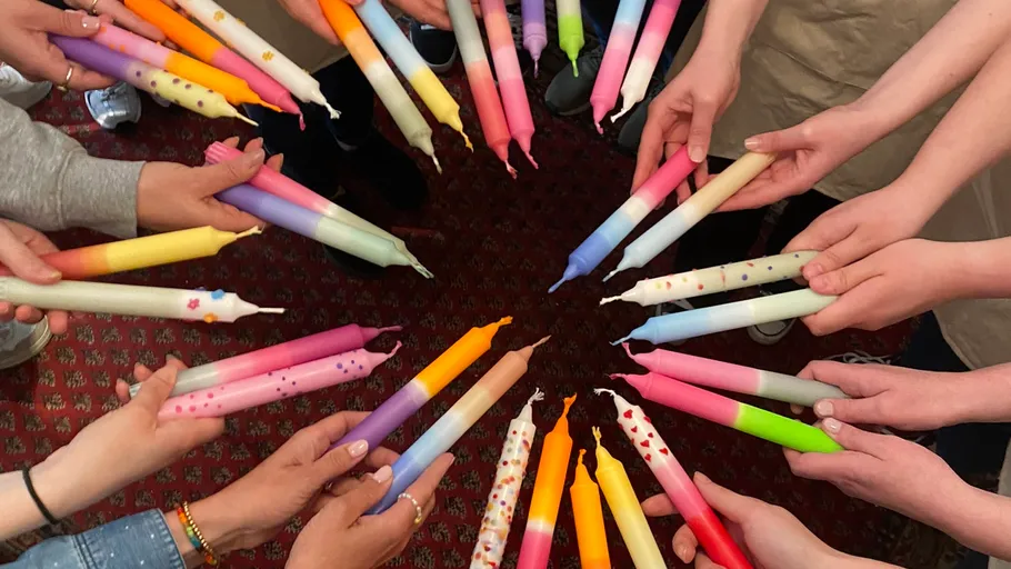 Hands holding colorful candles in a circle.