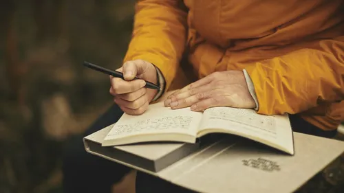 Person writing in notebook, outdoor setting.