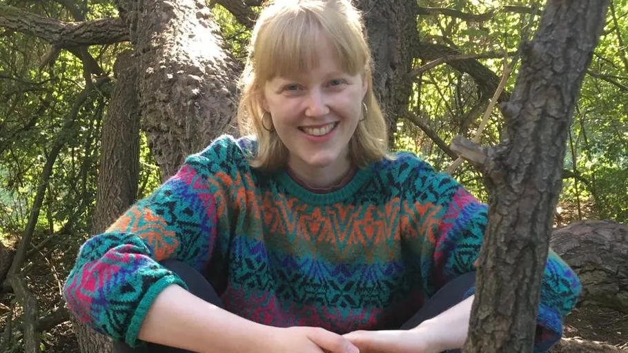Person sitting outdoors among trees smiling.