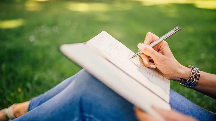Person writing in notebook on grass.