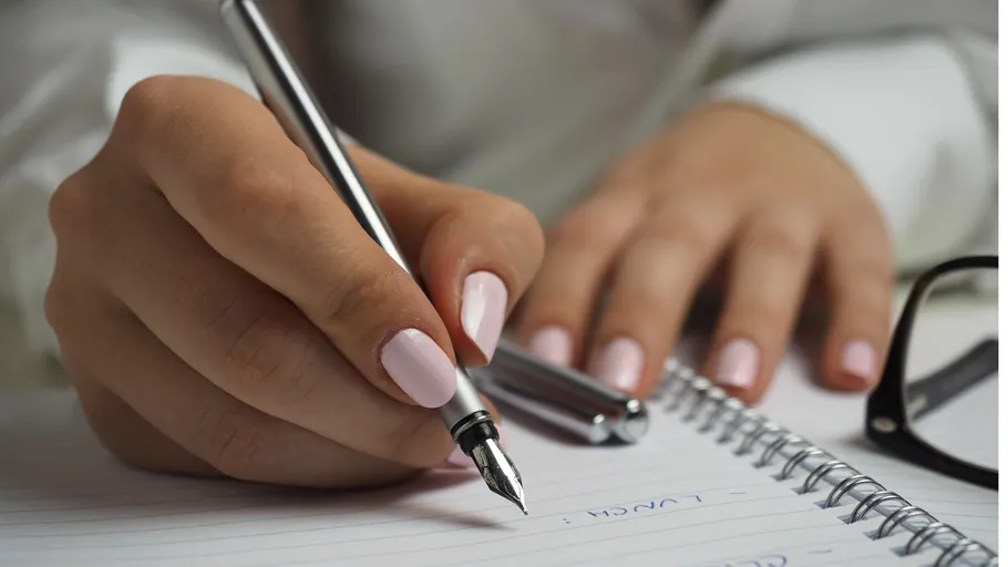 Hand schreibt mit Stift in Notizbuch.