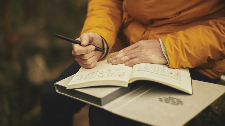 Person schreibt Notizen in ein Buch im Freien.