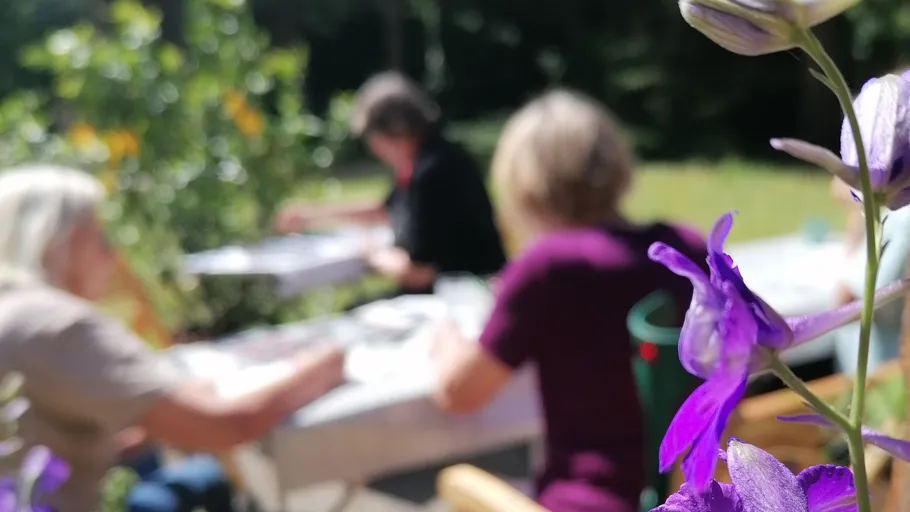 Personen malen im Freien, lila Blume im Vordergrund.