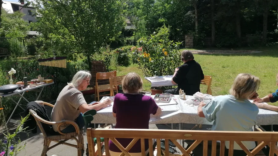 People sitting outdoors, crafting at tables in garden.