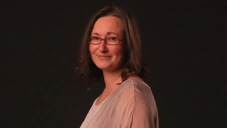 Frau lächelt vor dunklem Hintergrund.