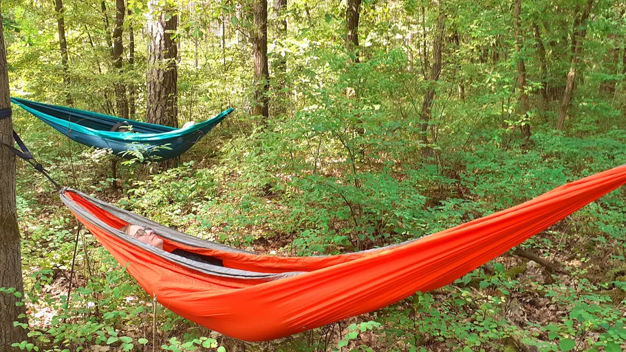Two hammocks in a forest, people relaxing.