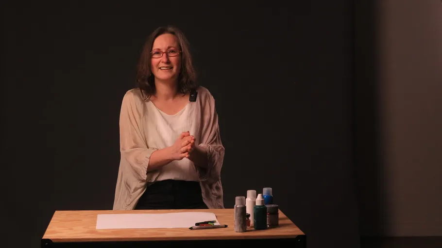 Frau lächelnd, steht am Tisch mit Kunstbedarf.