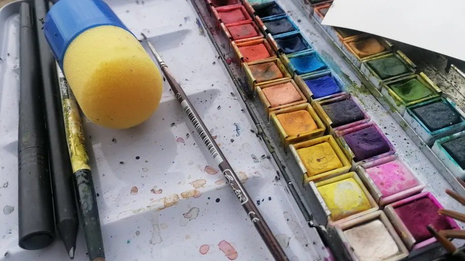 Wasserfarben und Malutensilien auf einem Tisch.