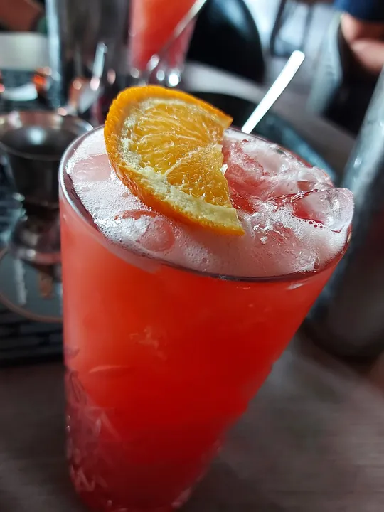 Red cocktail with orange slice garnish, indoors.