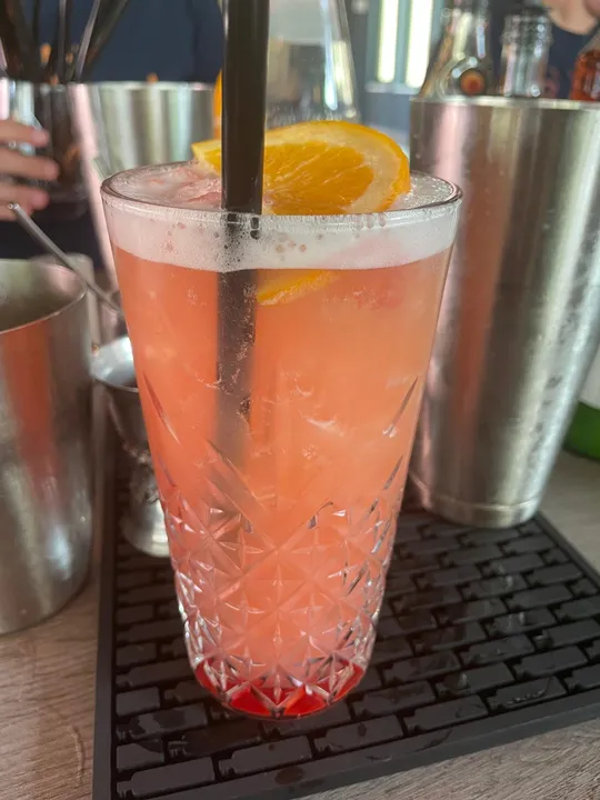 Orange cocktail with ice, straw, bar background.