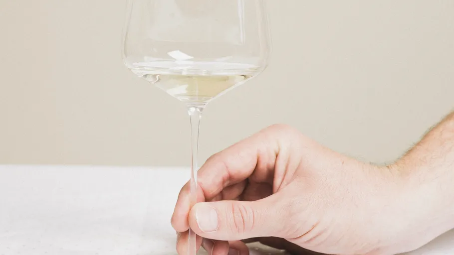 Hand hält ein Glas Weißwein.