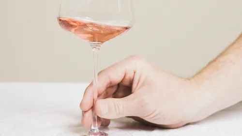 Hand holding wine glass on table.