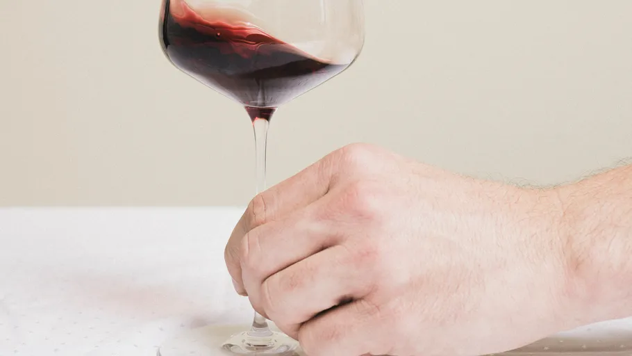 Hand holding wine glass on table.