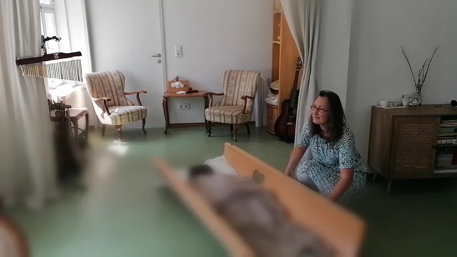 Woman kneeling beside a wooden coffin indoors.