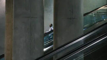 Man on escalator between large pillars.