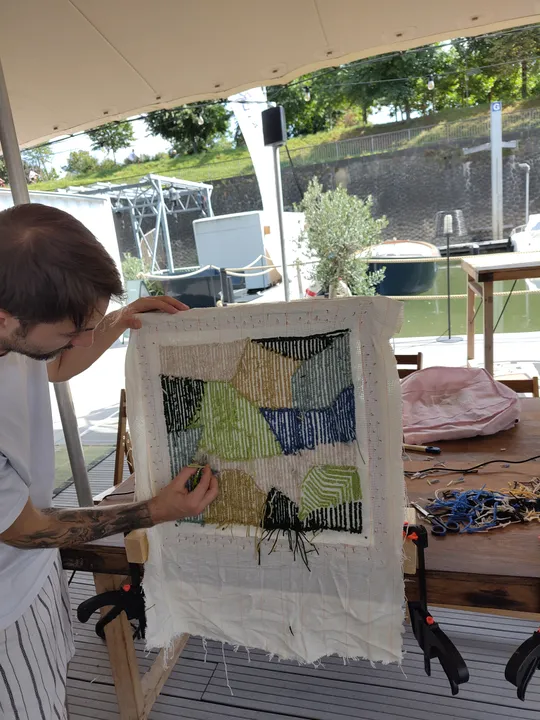 Person stickt buntes Stoffkunstwerk drinnen.