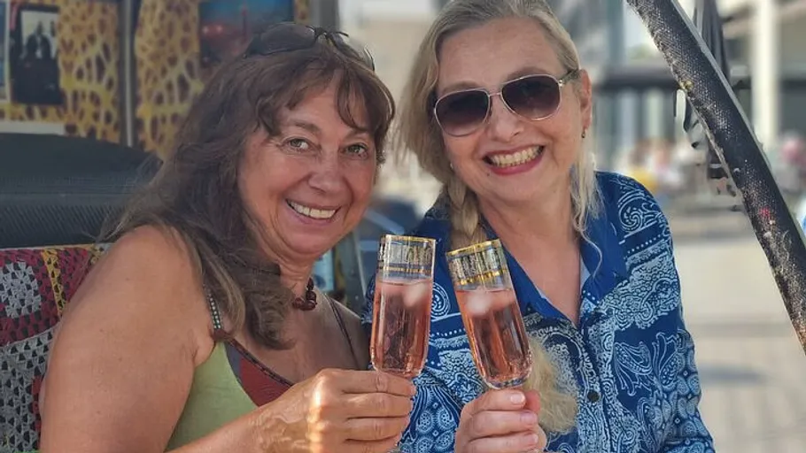 Two women smiling, holding drinks, outdoors.