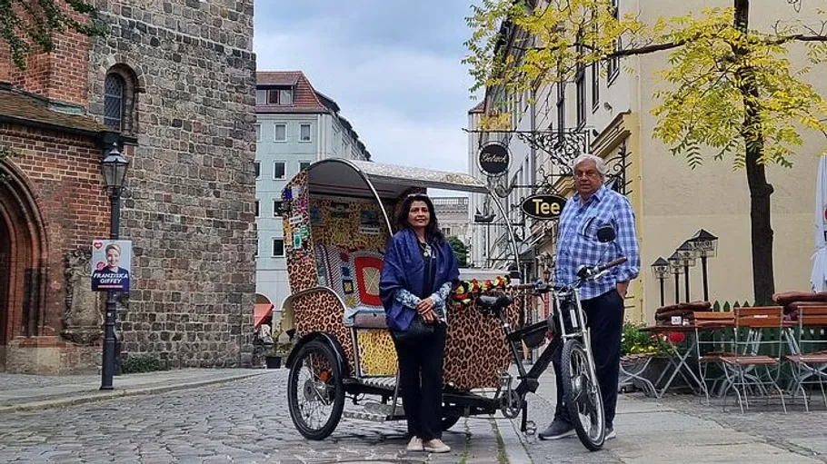 Two people with a rickshaw on cobblestone street.