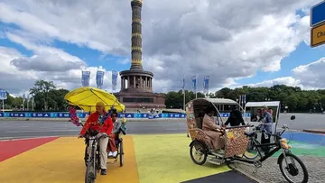 Cyclists with rickshaws near a large column monument.