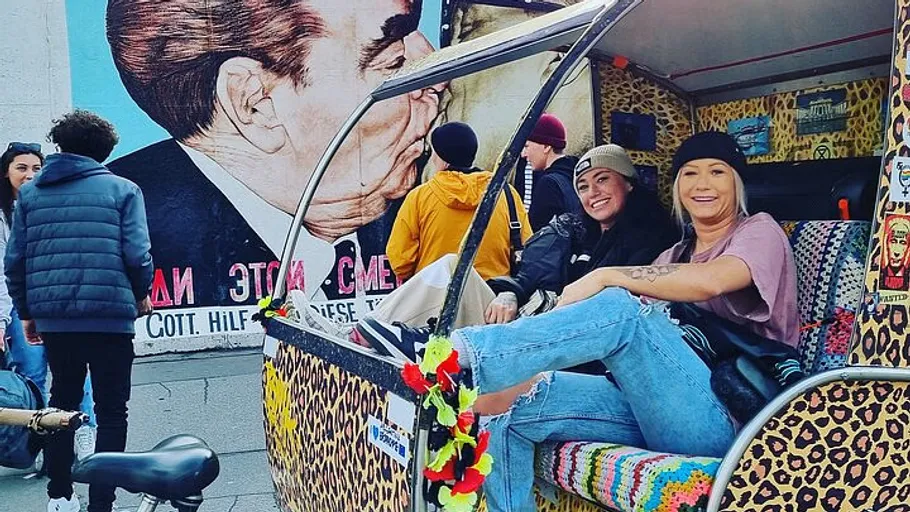 Two women sitting in colorful vehicle, mural behind.