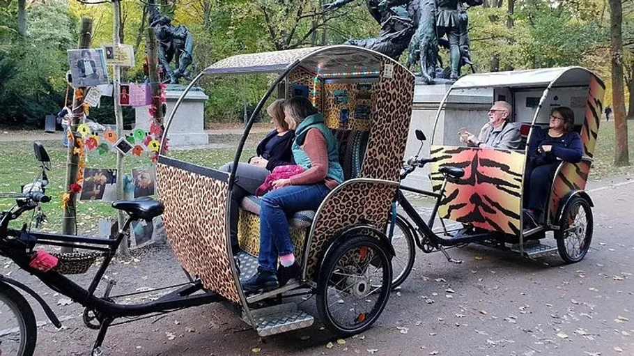 Two decorated rickshaws with passengers in park.