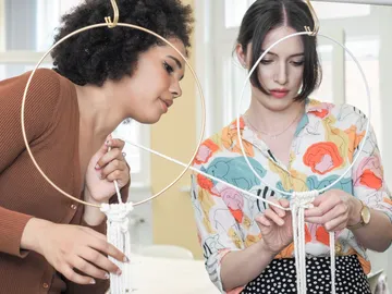 Zwei Frauen knüpfen gemeinsam dekorative Ringe aus Faden.