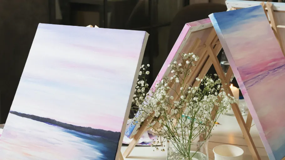 Paintings on easels, lit candle, flowers nearby.