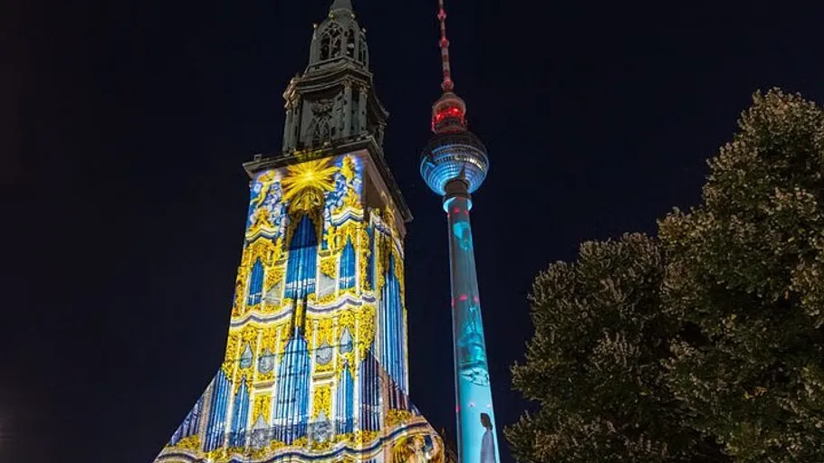 Church tower illuminated with colorful projections at night.