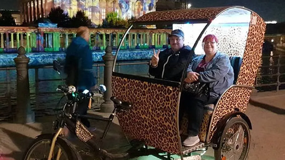 Two people in a leopard-print rickshaw at night.