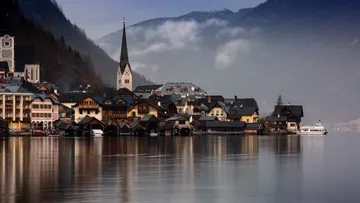 Village with church by misty lake and mountains.