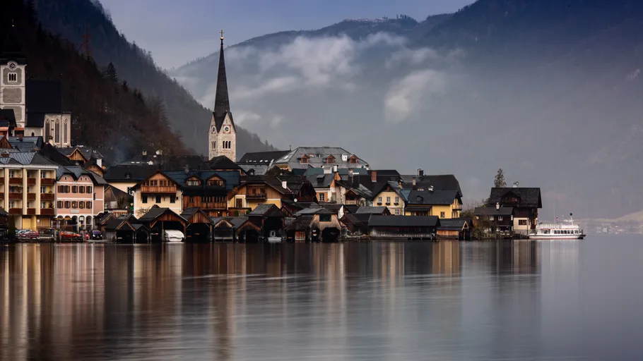 Dorf mit Kirche am nebligen See und Bergen.