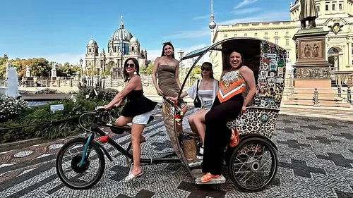 Four women pose on rickshaw in city square.