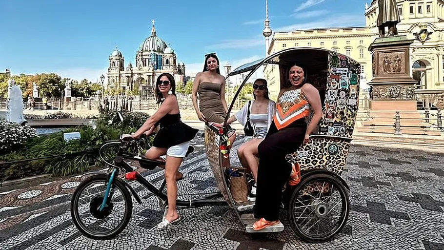 Four women pose on rickshaw in city square.